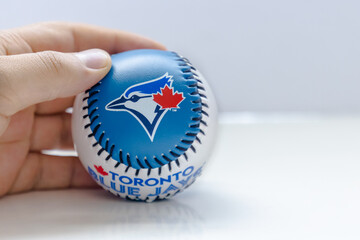 Fototapeta premium Calgary, Alberta, Canada. Aug 9, 2022 A person holding a Blue Jays baseball on a white background and table