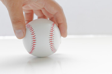 A person holding a baseball on a white background and table