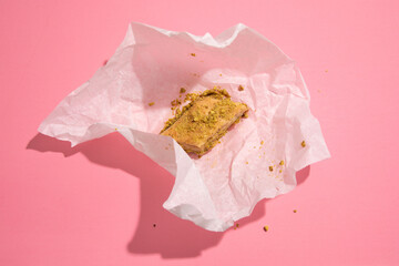 One piece of baklava traditionally wrapped in paper on pink background, top view