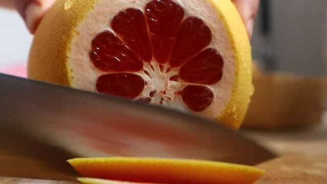 Woman's hands cut grapefruit on the board