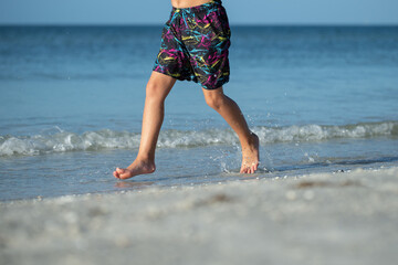 Boy running or walking at water edge splashing on beach in Florida