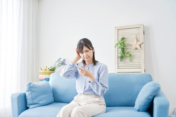 自宅でスマホを持って悩む女性