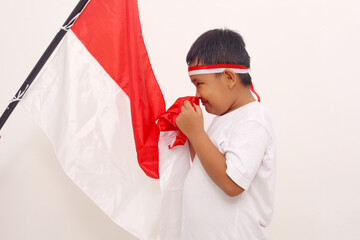 Asian boy standing while kissing indonesian flag with salute gesture. Independence day concept