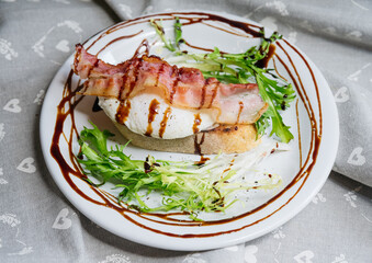 Delicious light breakfast poached egg on bruschetta with bacon, frisee salad and balsamic sauce dressing.