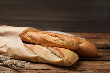 Fresh tasty baguettes and spikelets on wooden table, closeup