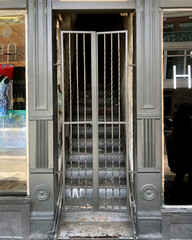 Stairs to an apartment behind a grey painted iron gate that leads to a busy city street 
