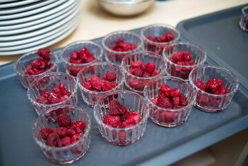 Many glass ramekins with fresh raspberries in them, the process of making dessert