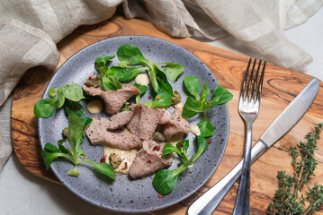 Thinly sliced baked ham with cream sauce and corn salad lettuce leaves. A portion on a plate.