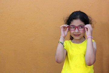 Hispanic 6-year-old girl shows her red glasses that she wears because she has astigmatism and...