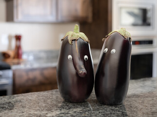Anthropomorphic eggplants hanging out together on a granite counter in the kitchen