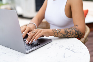 Beautiful young female hipster freelancer working with a laptop in a street cafe, writing an article, concentrated on work, close shot of hands