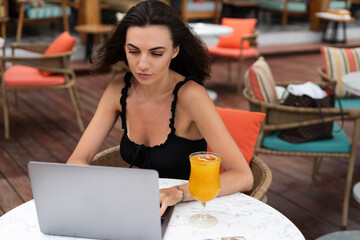 Beautiful young female hipster freelancer working with a laptop in a street cafe, writing an article, concentrated on work