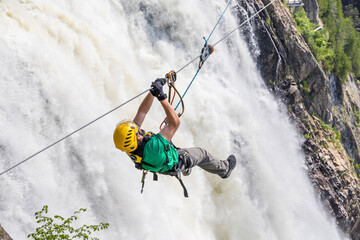 Man on a zipline going past a waterfall