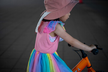オレンジ色の自転車に乗る虹色のワンピースを着た少女