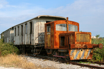 Fototapeta na wymiar Vecchio treno arruginito e abbandonato, su binario, composto da locomotore diesel e vecchi vagoni di legno.