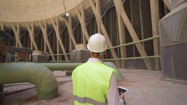 Engineer walking inside the cooling tower.
Engineer in white helmet walking through cooling tower working with his tablet.
