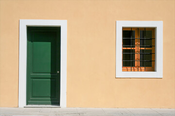 Facciata di edificio nuovo, casa  appena restaurata, composta da una finestra sbarrata e una porta verde con muro giallo.