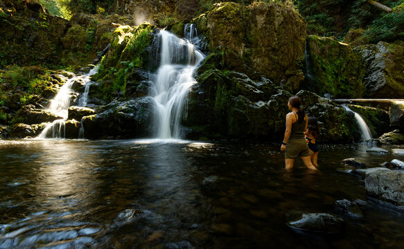 Mother and daughter wading in a river pool watching a cascading waterfall at Little Mashel Falls in Eatonville, Washington.
