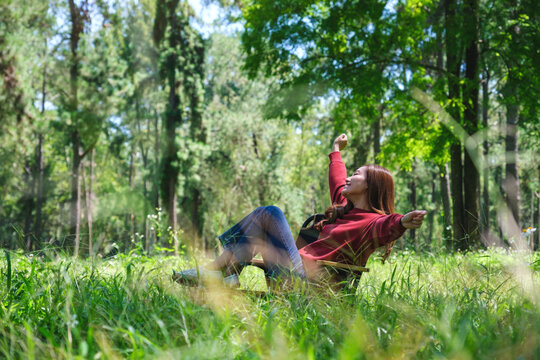 Portrait image of a beautiful young woman stretching arms while sitting and relaxing on a chair in the park