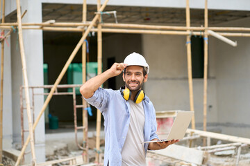 Naklejka na ściany i meble Foreman wear helmet and laptop and smile on construction site