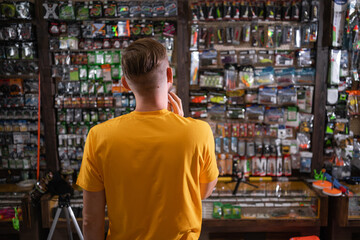 Back view of bearded man standing near showcase with fishing equipment in sports shop.