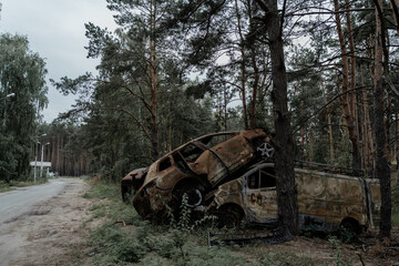 Fototapeta na wymiar Burnt cars in the city of Irpin stand on the side of the road near a pine forest