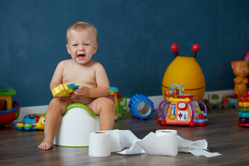 Cute smiling baby boy sitting on chamber pot with toilet paper rolls. Potty training. Domestic life