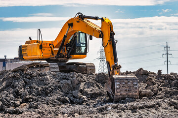 A powerful caterpillar excavator digs the ground against the blue sky. Earthworks with heavy equipment at the construction site. © Anoo