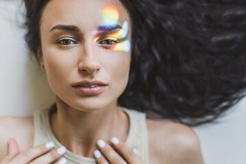 Portrait of trendy glamour brunette woman with fashion makeup and scatter gloss curly wave long hair laying down on the floor. Beautiful woman closed eyes and touching face  