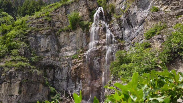 Jib up from bush to reveal waterfall on rocky cliff, Stewart Falls, Provo Utah