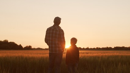 Farmer and his son in front of a sunset agricultural landscape. Man and a boy in a countryside field. Fatherhood, country life, farming and country lifestyle.