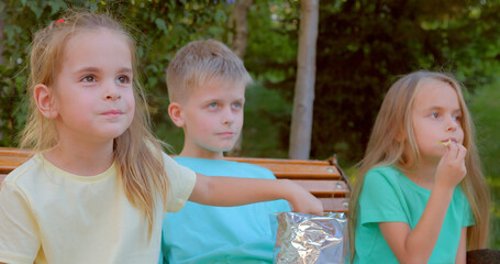 Three pretty kids eat delicious chips outdoor.
