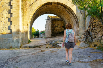 Fototapeta na wymiar Tourist woman crossing an old stone bridge at the entrance of a village in Castile, Puente Congosto.