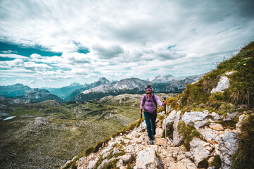 Fototapeta premium Young woman is hiking on beautiful trail with flowers from Baires Lake to Seekofel in the Dolomite mountains in the morning. Seekofel, Dolomites, South Tirol, Italy, Europe.