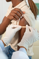 Close-up of hands of nurse in protective gloves applying plaster to female arm. Doctor putting patch on shoulder of patient after injection. Vaccination and immunization concept