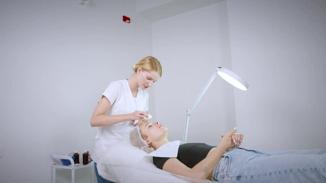 Вeautician cosmetologist doing procedure fractional microneedle mesotherapy with Dermapen. Hardware cosmetology in clinic salon for client. 