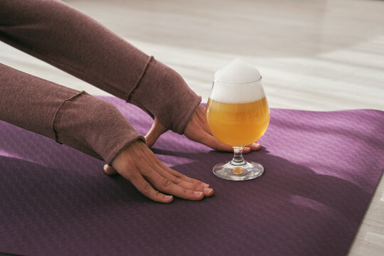 Crop Unrecognizable Female Doing Asana On Mat With Glass Of Beer During Yoga Session In Light Living Room At Home