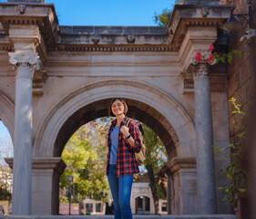 travel to Turkey. Happy asian female tourist traveller with backpack walks in old city. Woman against backdrop of Hadrian's gate - popular attraction in old city of Antalya