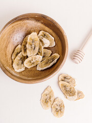 Banana chips in wooden bowl on white background. Fried bananas