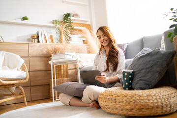 Smiling Asian freelance business women casual wear sitting on sofa using laptop looking at screen typing message,working call video conference in living room.Happy young girl relax at home in summer