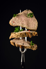 Sliced smoked ham with parsley on a fork on a black background. A natural product from an organic farm, produced using traditional methods