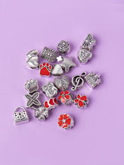 Assorted metal charms for bracelets on purple background. Butterfly, flowers, crown, owl, heart. Creating jewelry