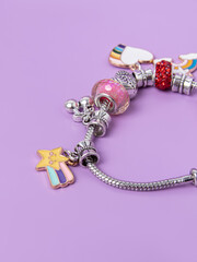 Silver charm bracelet with many charms on purple background. Creating jewelry. Children's bracelets close up