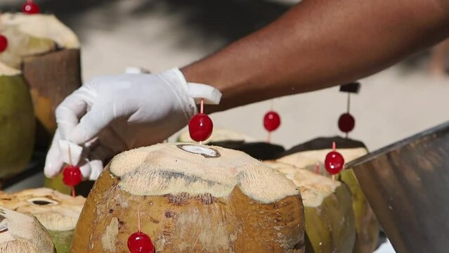 The barman's hand in a disposable glove decorates coconut cocktails with a piece of coconut and a cherry.Preparation of an exotic cocktail in coconut.The concept of a beach holiday in a hotel
