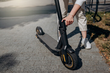 Obraz premium Close up of woman in white suit folding her electro scooter after ride while standing in city parkland