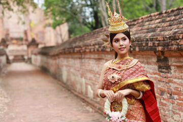 Young fashion and beautiful asian woman wearing Thai red traditional costume holding jasmine flower garland with happy and peace standing outdoor in ancient temple Ayutthaya, Thailand. Travel concept