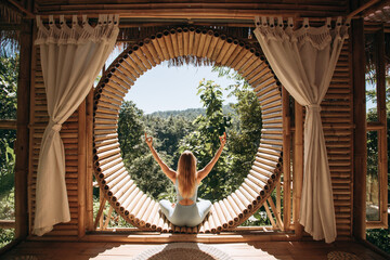 An attractive slim woman practices yoga in a bamboo house in Bali. The concept of fitness, sport, training and lifestyle. Yoga in a beautiful place.