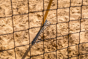 ein Netz vor dem Volleyball Platz verdeckt den Rechen der auf dem gelben Sand steht