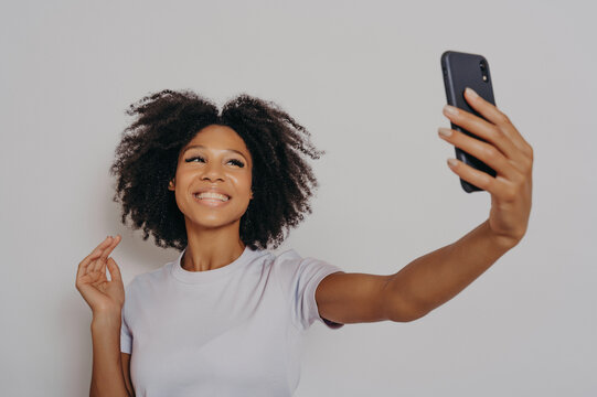 Positive cheerful dark skinned female making photo on modern smartphone camera