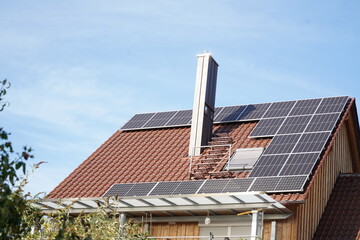 Solar panels on a residential building roof. The high chimney casts shadows on a module